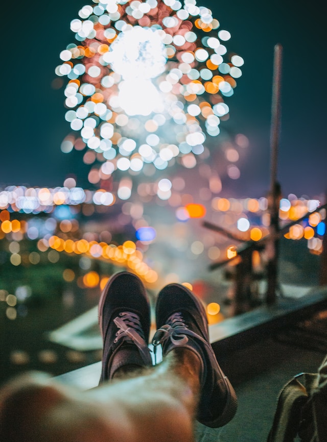 Foto che ritrae piedi appoggiati in posizione di relax, sullo sfondo fuochi d'artificio